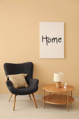 Gri koltuk ve bej duvarın yanındaki kahve masası. Posterli.