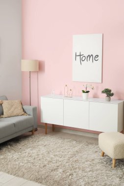 Oturma odasında rahat gri kanepe, beyaz dolap ve poster var.