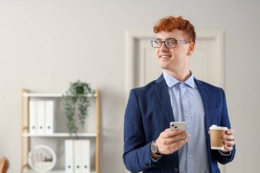 Ofisinde bir fincan kahve ve cep telefonu olan genç kızıl iş adamı.