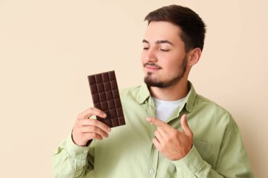 Genç adam bej arka plandaki lezzetli çikolatayı işaret ediyor.