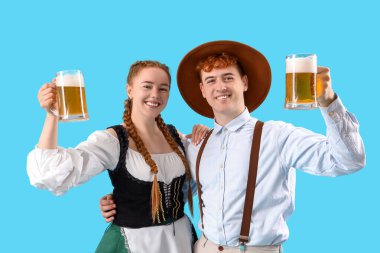 Geleneksel Alman elbiseli genç bir çift mavi arka planda bira ile