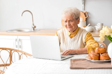 Üst düzey kadın mutfaktaki masada dizüstü bilgisayar kullanıyor.