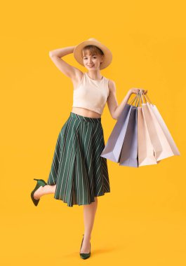 Sarı arka planda alışveriş torbaları olan güzel, mutlu genç bir kadın.