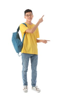 Sırt çantalı mutlu Asyalı erkek öğrenci beyaz arka plandaki bir şeyi işaret ediyor.