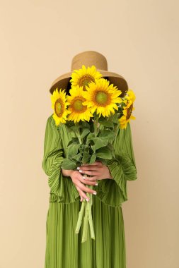 Young woman with beautiful sunflowers on beige background