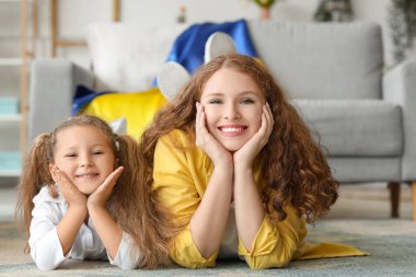 Ukrayna bayrağıyla küçük mutlu bir kız ve annesi oturma odasında yerde yatıyor.