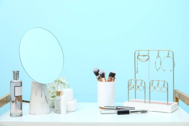 Farklı dekoratif kozmetik ürünler, beyaz masa üzerinde ayna ve mücevherler.