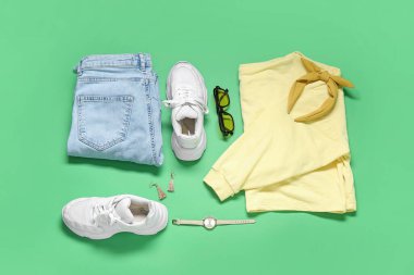 Yeşil arka planda şık kadın kıyafetleri, aksesuarları ve spor ayakkabıları olan kompozisyon