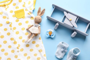 Bebek kıyafetleri, emzik ve renkli arka planda oyuncaklarla kompozisyon