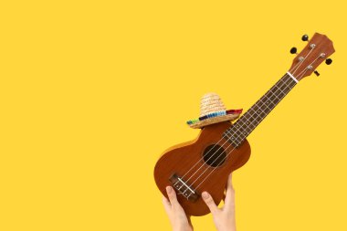 Sarı arka planda sombrero ile ukulele tutan kadın elleri