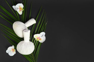 Bitkisel masaj torbaları, orkide çiçekleri ve arka planda palmiye yaprağı olan kompozisyon