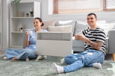 Evde kaloriferin yanında çay ısıtan genç bir çift.