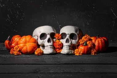 Siyah ahşap masa üzerinde kafatası, kabak ve kadife çiçekli Cadılar Bayramı kompozisyonu