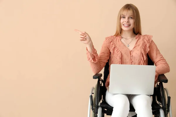 車椅子のラップトップを持つ若い女性は ベージュの背景に何かを指差しています — ストック写真