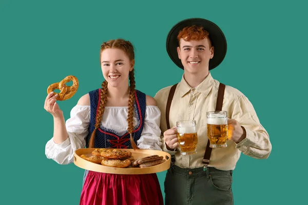 Young couple in traditional German clothes with beer and snacks on green background
