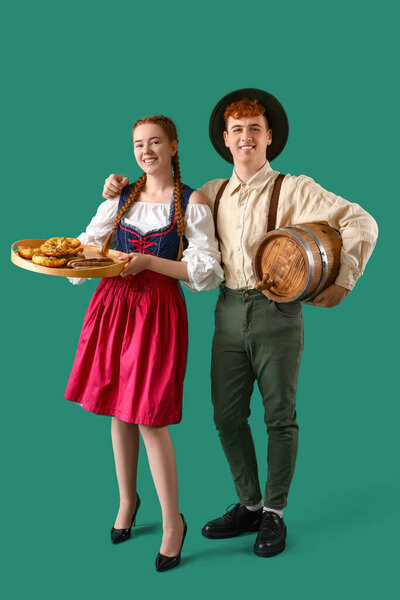 Молодая пара в традиционной немецкой одежде с пивом и закусками на зеленом фоне