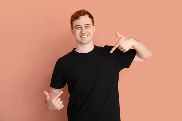 Junger Mann Zeigt Auf Sein Schwarzes Shirt Auf Beigem Hintergrund — Stockfoto