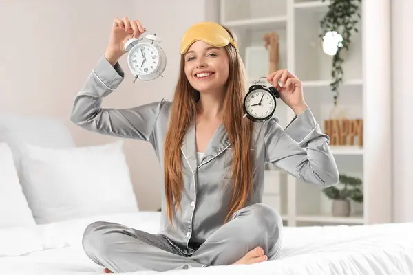 自宅でベッドに目覚まし時計が付いているパジャマの幸せな若い女性 — ストック写真