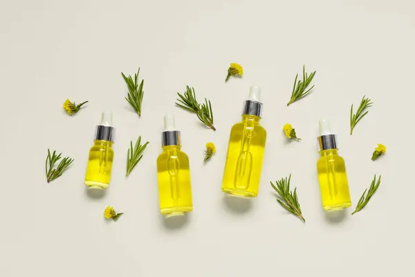 stock image Bottles of healthy essential oil with herbs and flowers on light background