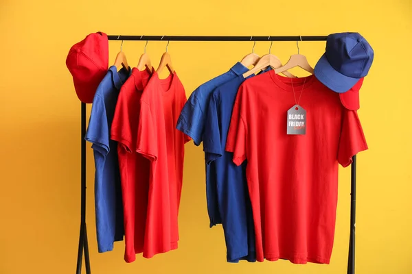 Rack with different t-shirts and caps on yellow background. Black Friday sale
