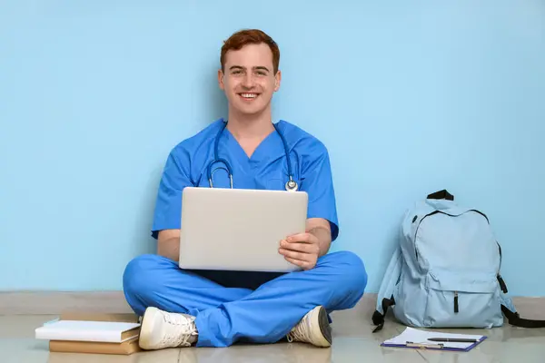 Male medical student studying with laptop near blue wall