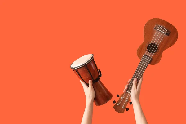 Female hands holding drum and ukulele on orange background