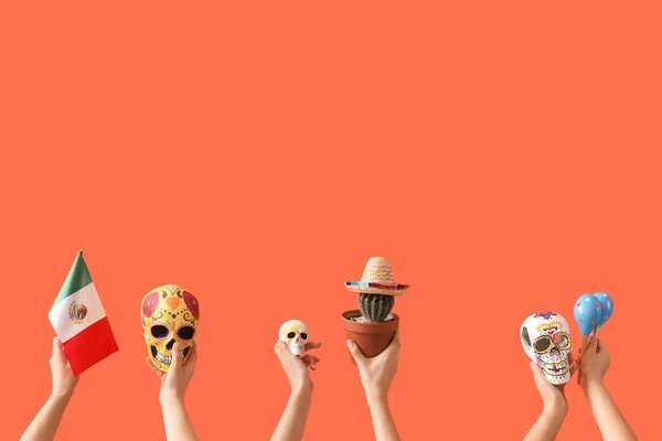 Female hands holding painted skulls, Mexican flag, cactus and maracas on orange background
