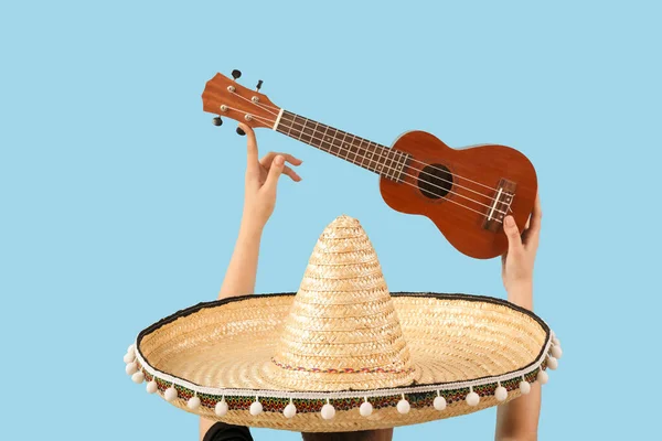 Female hands holding sombrero and ukulele on blue background