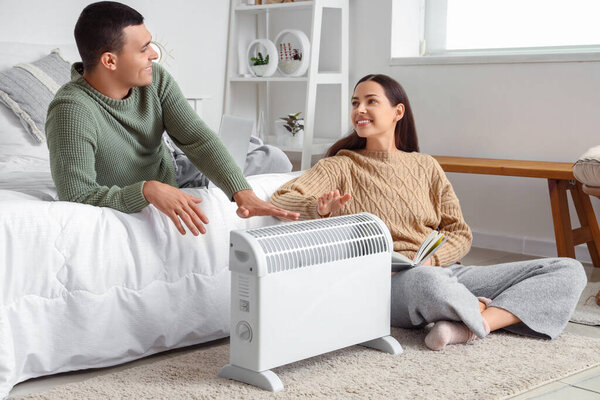 Young couple warming hands near radiator in bedroom