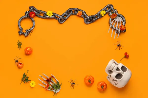 Frame made of skull, shackles, skeleton hands and marigold flowers for Halloween celebration on orange background