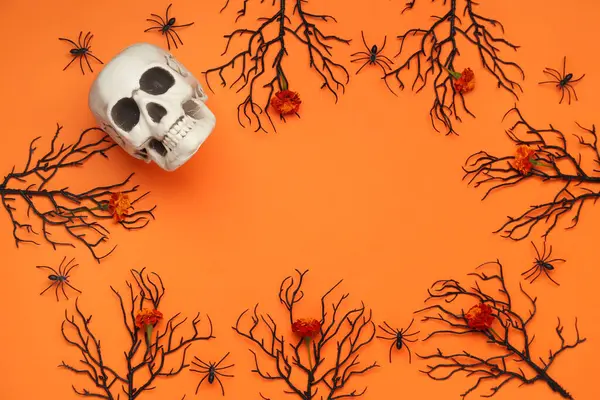 Frame made of skull, branches and marigold flowers for Halloween celebration on orange background