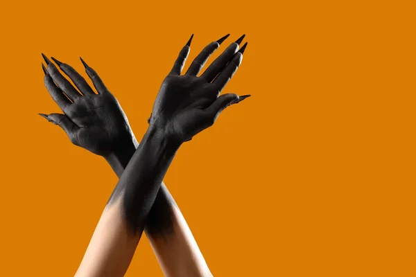 Black hands of witch with claws on orange background. Halloween celebration