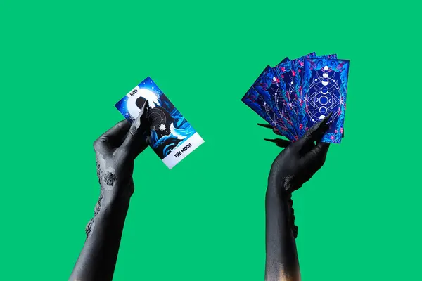 Black hands of witch with Tarot cards on green background. Halloween celebration