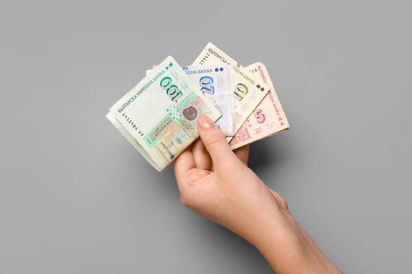 Female hand holding Bulgarian lev banknotes on grey background