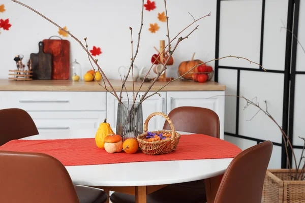 Dining table with vase, Halloween pumpkins and candies in festive kitchen