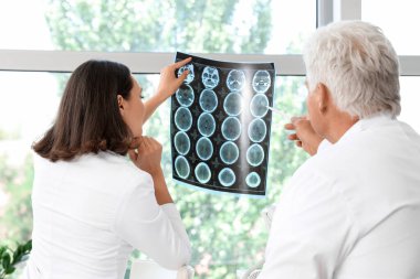 Doktorlar pencerenin yanındaki muayenehanede röntgen taramasını inceliyor.