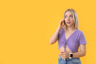 Sarı arka planda cep telefonuyla konuşan düşünceli genç ve güzel bir kadın.