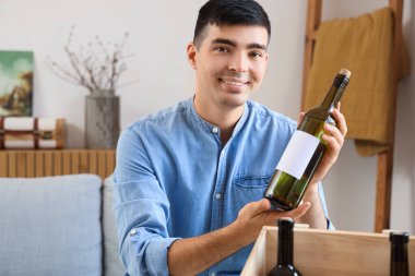Evde şarap şişesi olan genç bir adam var.