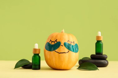 Göz altı yamalı balkabağı, spa taşları, serum ve yeşil arka planda yapraklar