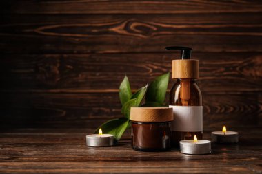 Kremalı kavanoz, mumlar ve tahta arka planda bir şişe şampuan.