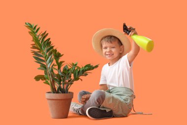 Küçük sevimli bahçıvan sprey şişesiyle turuncu arka planda oturuyor.