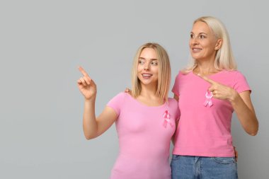 Pembe kurdeleli kadınlar gri arka plandaki bir şeyi işaret ediyorlar. Göğüs kanseri farkındalığı konsepti