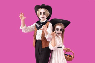 Cadılar Bayramı için giyinmiş küçük çocuklar ve mor arka planda şekerler.