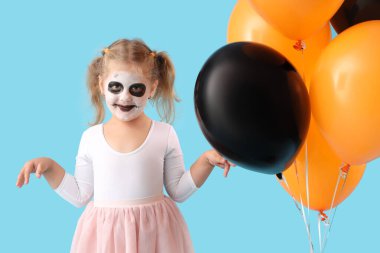 Cadılar Bayramı için giyinmiş küçük kız mavi arka planda balonlarla