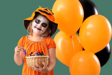 Cadılar Bayramı için giyinmiş küçük bir kız. Yeşil arka planda balonlar ve şekerlerle.