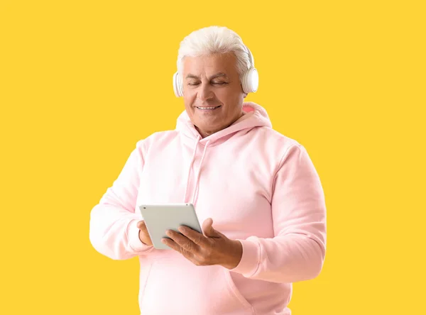 Senior man in headphones using tablet computer on yellow background
