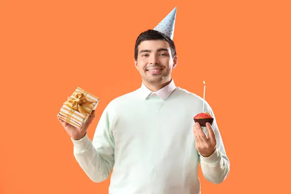 Happy young man with birthday muffin and gift on red background