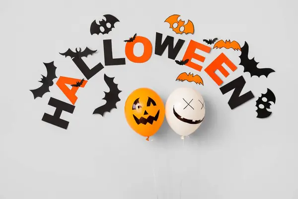 Word HALLOWEEN with balloons and paper bats on light background