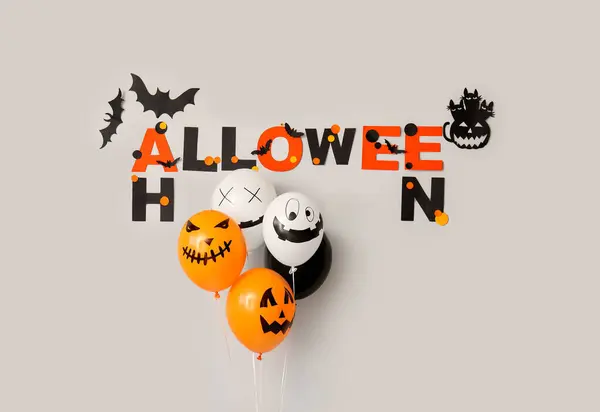 Word HALLOWEEN with balloons and paper decor on light background