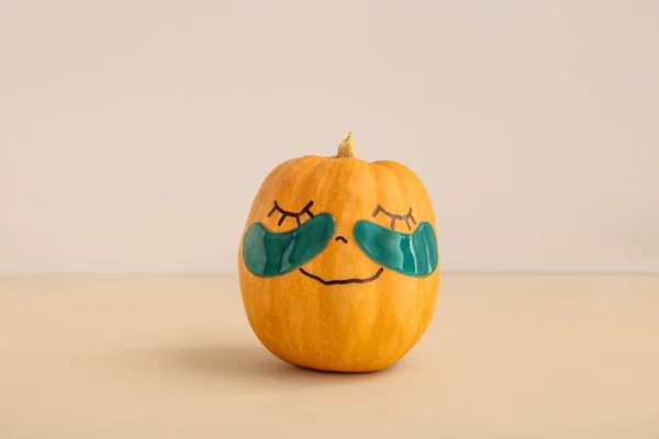 Pumpkin with drawn face and under-eye patches on beige background